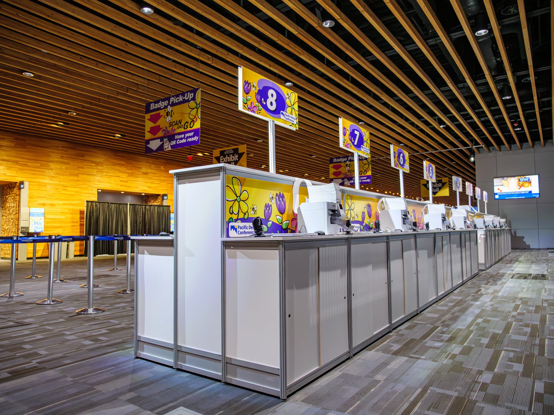Wide view of the Pacific Dental Conference registration counter at the Vancouver Convention Centre, with branded number signs hanging above each station.