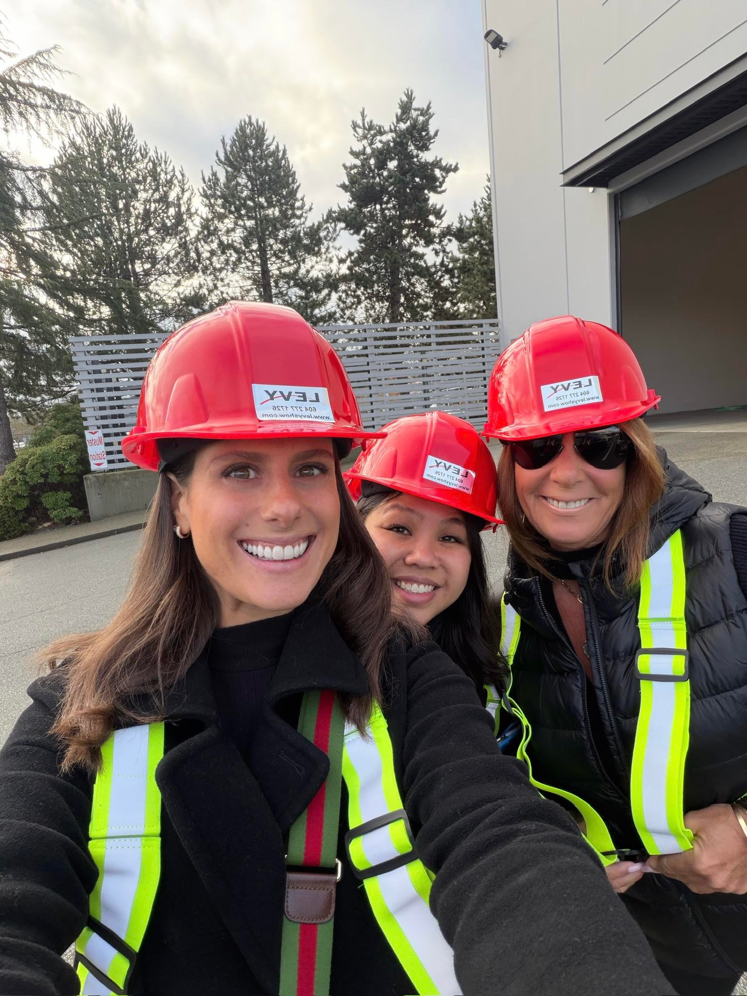 Three members of the LEVY leadership team in red LEVY hard hats and high-visibility vests outside the company’s Richmond warehouse.