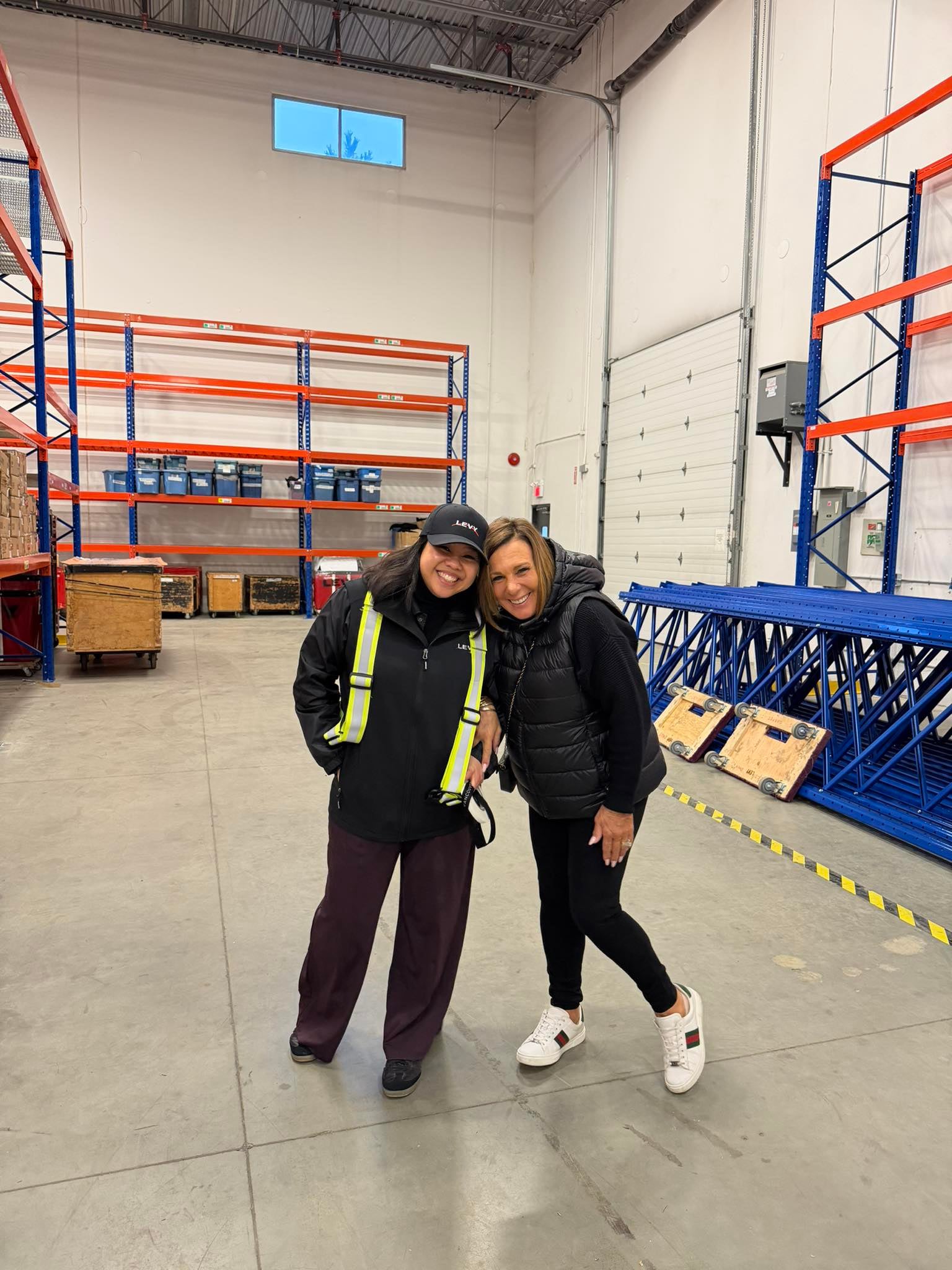 Two LEVY leaders inside the Richmond warehouse, with blue-and-orange pallet racking behind them.